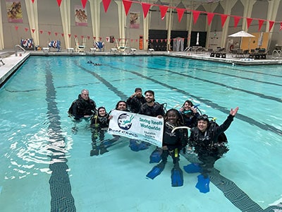 Divers holding Reef Check sign during dive training activity in swimming pool.