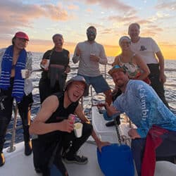 Group of divers and researchers celebrating coral reef conservation on a boat at sunset.