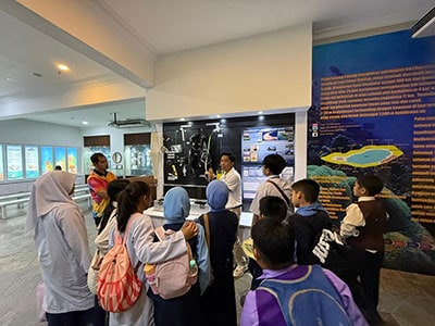 A group of students and educators learn about coral reef ecosystems and conservation initiatives at an educational display.